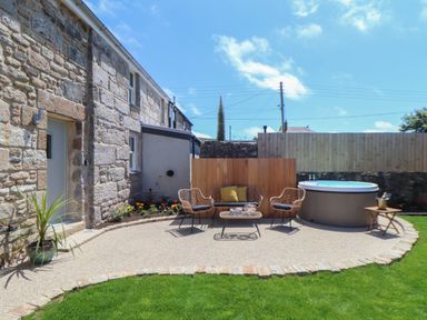 A stone house with a paved patio with outdoor seating and a hot tub at Victory View in Pendeen