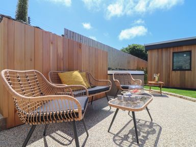 An outdoor patio area with wicker chairs a table with cups a wooden fence and a small wooden building at Victory View in Pendeen
