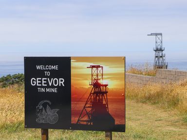 A sign welcoming visitors to Geevor Tin Mine with a sunset image of a mining structure and an ocean in the background at Victory View in Pendeen