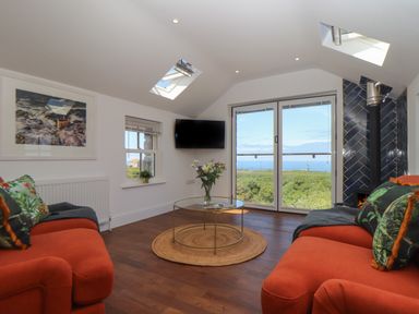 A living room with two orange sofas a glass coffee table and a wood burning stove at Victory View in Pendeen