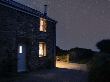 A stone house with lit windows under a starry sky at Victory View in Pendeen