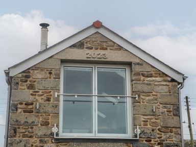Front view of a stone house with large window marked 2023 and metal chimney at Victory View in Pendeen