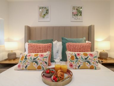 A bed with decorative pillows and a tray of breakfast items between two lamps on bedside tables at Victory View in Pendeen