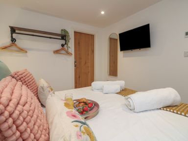 A bedroom with a bed with pillows towels and breakfast tray a wall mirror television wooden door and wall hangers at Victory View in Pendeen