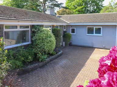 An outdoor paved driveway area with shrubs and a building with windows and a tiled roof at Sweden Bridge Cottage in Ambleside