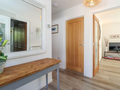 A hallway with a wooden table and a large wall mirror next to a closed wooden door and an open door leading to a living room at Sweden Bridge Cottage in Ambleside