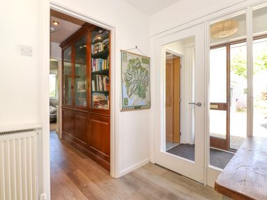 A hallway with wooden floor a glass door a wooden cabinet with books and a map on the wall at Sweden Bridge Cottage in Ambleside