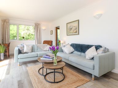 A living room with two light blue sofas a round wooden coffee table with flowers and books by a window at Sweden Bridge Cottage Ambleside