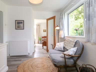 A room with a cushioned wooden armchair beside a window with curtains and a lamp near a round woven rug at Sweden Bridge Cottage in Ambleside