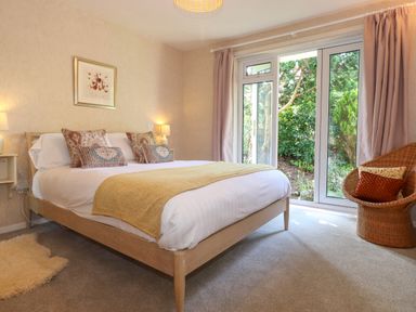 A bedroom with a bed a wicker chair and glass doors opening to a garden at Sweden Bridge Cottage Ambleside