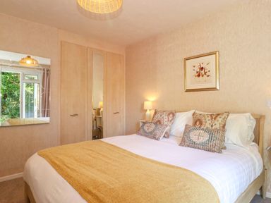 A bedroom with a double bed pillows a yellow throw blanket a wooden wardrobe a mirror and a lamp at Sweden Bridge Cottage in Ambleside