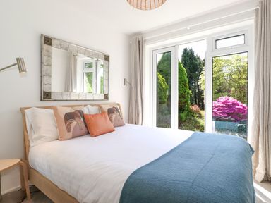 A bedroom with a bed with pillows and a blue throw near large windows showing a garden at Sweden Bridge Cottage in Ambleside