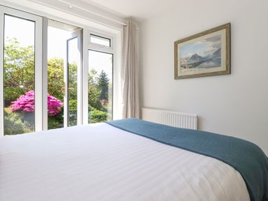 A bedroom with a bed near glass doors opening to a garden with flowering bushes at Sweden Bridge Cottage in Ambleside
