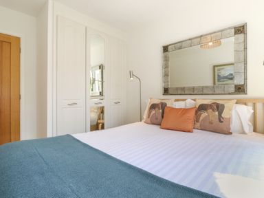 A bedroom with a bed with pillows a blue blanket a floor lamp a large wall mirror and a wardrobe at Sweden Bridge Cottage in Ambleside