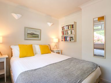 A bedroom with a bed with yellow pillows two bedside tables with lamps a bookshelf and a wall mirror at Sweden Bridge Cottage in Ambleside