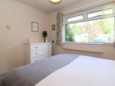 A bedroom with a bed covered with a gray blanket and a white chest of drawers with flowers on top at Sweden Bridge Cottage in Ambleside