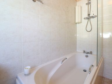 A bathtub with metal handles and a showerhead in a tiled bathroom at Sweden Bridge Cottage in Ambleside
