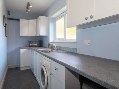 A narrow laundry room with a washing machine under a gray countertop and white cabinets on a blue wall at Sweden Bridge Cottage in Ambleside