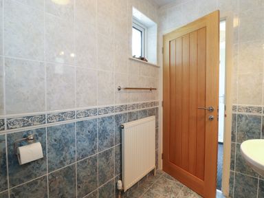 A bathroom with blue and white tiled walls a wooden door a small window a radiator a toilet paper holder and a sink at Sweden Bridge Cottage in Ambleside