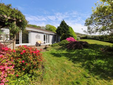 A garden with flowering bushes and a bench next to a single-story house at Sweden Bridge Cottage in Ambleside