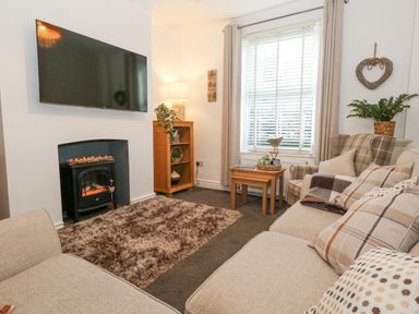 A living room with a sofa an armchair a television mounted on the wall and a small fireplace at Garibaldi Cottage in Weymouth