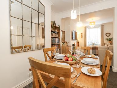 A dining area with a wooden table set for four and a living room with a window at Garibaldi Cottage in Weymouth