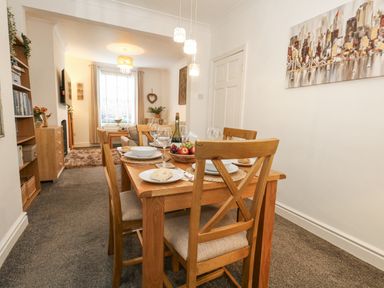 A dining area with a wooden table set for four and a living room with a sofa and window at Garibaldi Cottage in Weymouth