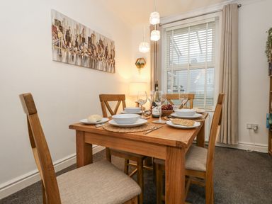 A dining room with a wooden table set for four with plates bread wine glasses and chairs at Garibaldi Cottage in Weymouth