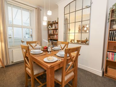 A dining room with a wooden table set for four and shelves with books at Garibaldi Cottage in Weymouth