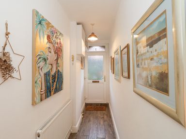 A hallway with framed pictures on walls a radiator and a white door at Garibaldi Cottage in Weymouth