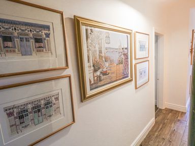 A hallway with framed artwork on the wall and a wooden floor at Garibaldi Cottage in Weymouth