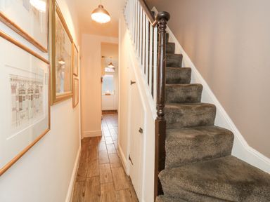 A narrow hallway with framed pictures on the wall and carpeted stairs on the right at Garibaldi Cottage Weymouth