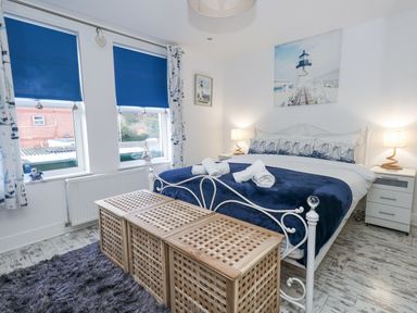 A bedroom with a white metal bed frame navy bedding and three wooden baskets at the foot of the bed with two bedside tables and blue window blinds at Garibaldi Cottage in Weymouth