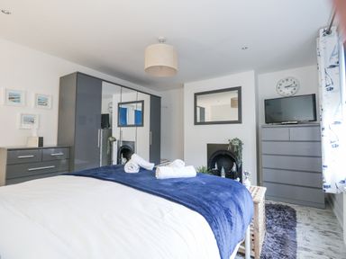 A bedroom with a bed covered with white and blue blankets and rolled towels on top at Garibaldi Cottage in Weymouth