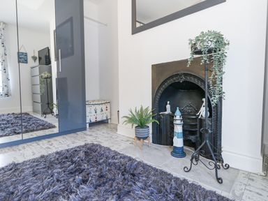 A room with a black fireplace decorated with plants and figures a mirrored wardrobe and a chest with a patterned fabric at Garibaldi Cottage in Weymouth
