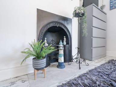 A black decorative fireplace with a potted plant and lighthouse ornament in front at Garibaldi Cottage in Weymouth