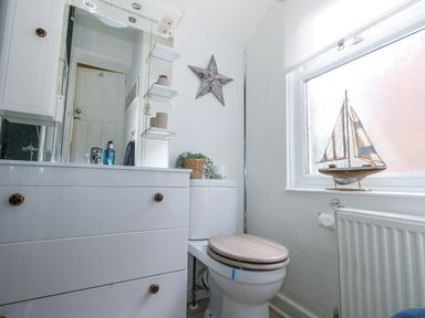 A bathroom with a toilet a vanity cabinet a window with a model sailboat and a star decoration on the wall at Garibaldi Cottage in Weymouth