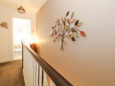 A hallway with a metal leaf wall decoration a wooden handrail and a doorway leading to a bright room at Garibaldi Cottage in Weymouth