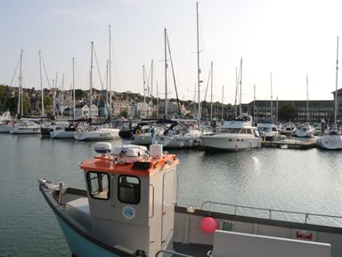 A marina with several sailboats and yachts docked with houses and buildings in the background at Garibaldi Cottage in Weymouth