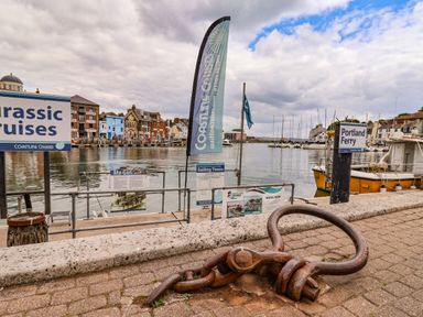 A harbor with boats docked along the quay and signs for Coastline Cruises and Portland Ferry at Garibaldi Cottage in Weymouth