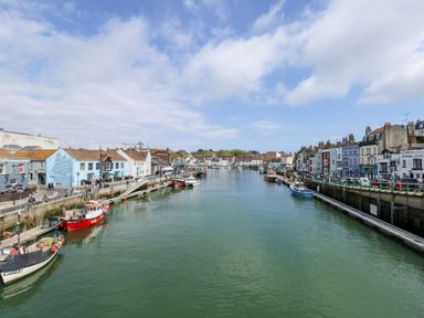 A harbor with boats docked along the waterfront and buildings on both sides at Garibaldi Cottage in Weymouth