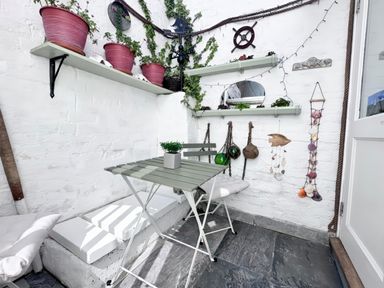 A small outdoor seating area with table and chairs and plants on shelves at Garibaldi Cottage in Weymouth