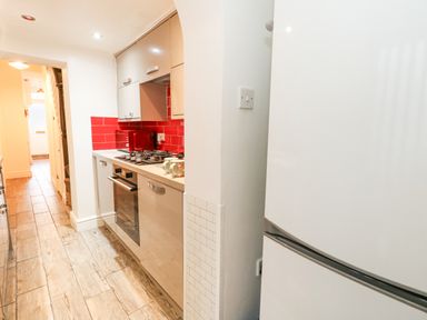 A narrow kitchen with white cabinets red tiled backsplash gas stove and wooden floor at Garibaldi Cottage in Weymouth