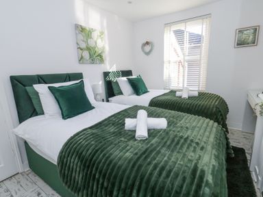 A bedroom with two single beds with green bedding and pillows at Garibaldi Cottage in Weymouth