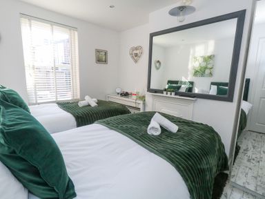 A bedroom with two single beds with green blankets and pillows next to a window and a large mirror at Garibaldi Cottage in Weymouth