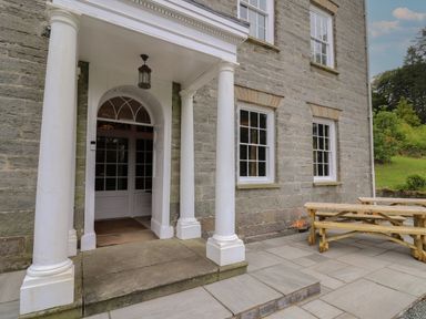 The entrance of a stone building with white columns and a wooden picnic table on the patio at Llwynderw Hall in Abergwesyn near Llanwrtyd Wells