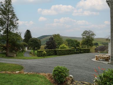 A gravel driveway leading to a garden area with trimmed hedges trees hills in the background at Llwynderw Hall in Abergwesyn near Llanwrtyd Wells