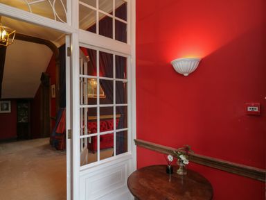 A hallway with a round wooden table with a flower vase and a wall light by a red wall at Llwynderw Hall in Abergwesyn near Llanwrtyd Wells