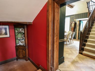 A corner cabinet with china dishes against a red wall next to a staircase and dining area at Llwynderw Hall in Abergwesyn near Llanwrtyd Wells