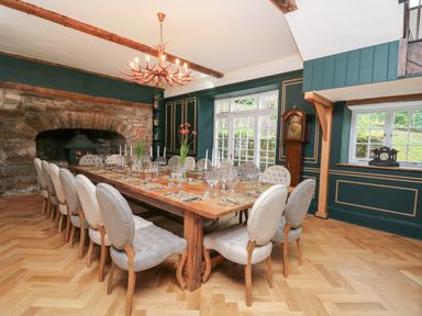 A dining room with a long wooden table set with glassware and candles with upholstered chairs around it at Llwynderw Hall in Abergwesyn near Llanwrtyd Wells